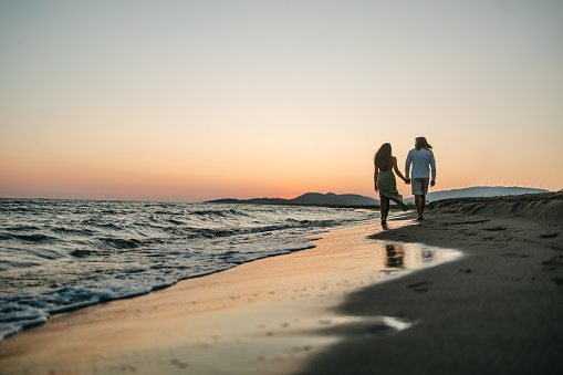 Low angle view of a couple walking by the sea in a romantic atmosphere at sunset