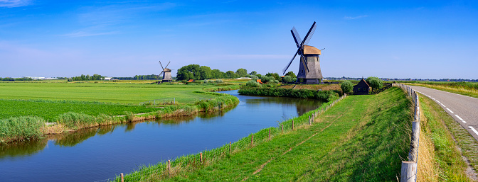 Dutch windmills along a canal with reed and a meadow alongside under a nicely clouded sky. The location is Schermerhorn, Netherlands.
