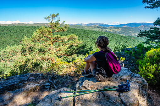 Woman hiker resting on a rock and contemplating the landscape, Guadarrama, Madrid