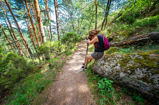 Woman hiker very tired and sitting on a rock on the road in the forest of Guadarrama, Madrid