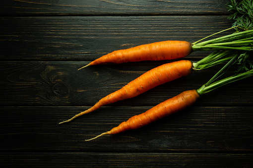 Three fresh and sweet carrots on a black kitchen table are ready to be added to a meal. Carrot diet concept.