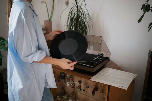 Close-up of a woman playing vinyl record on gramophone at home. Cropped shot of a female hands placing vinyl music disc on turntable.
