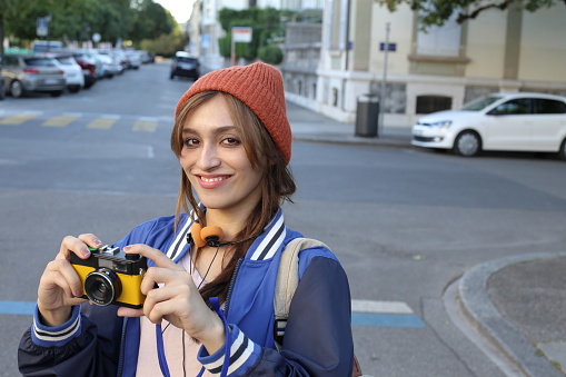 A cute South Asian female tourist is taking a picture with a yellow vintage camera. She is looking away contemplating something inspirational.