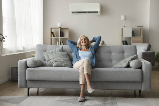 istock Cheerful old woman resting on grey soft couch under conditioner 1583406966