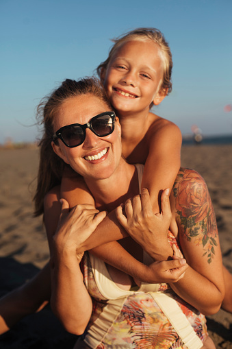 Mom with sunglasses poses for photos with her young son on a sandy beach