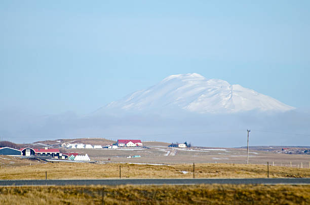Hekla volcano, Iceland, as last remnants of snow melt from farm fields in early spring. Fog around base of volcano. Typical stratovolcano shape. Dairy farms in foreground. From the south along Highway 1.