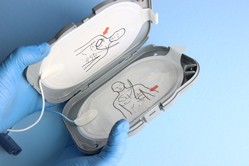 Defibrillator electrodes in the case beeing opened in a light blue background by a professional wearing gloves