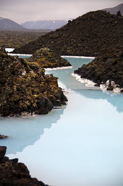 Blue Lagoon showing white silica deposits (chalcedony) on moss covered black lava rocks. Dissolved silica makes water look blue. As the hot water cools, the silica deposits on the native black lava rock. Grindavik, Iceland.