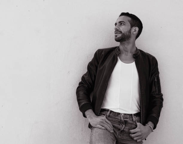 a handsome man looking away while leaning on a wall with hands in pockets | pride month