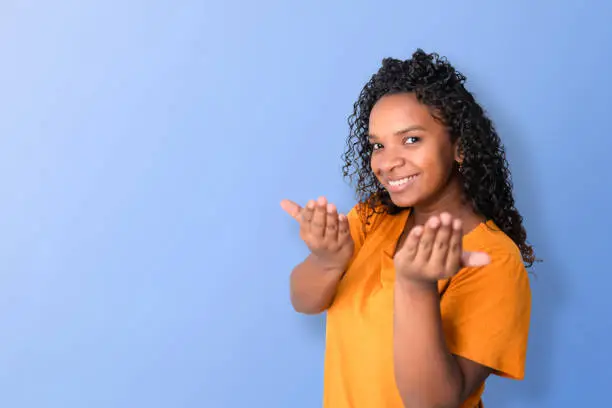 Black woman smiling and looking at camera, inviting to come with her hands, with blue background