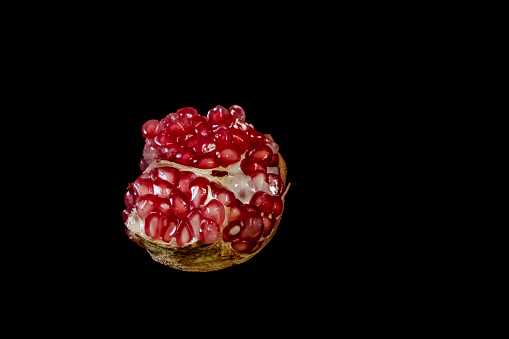 Close up of a freshly cut red pomegranate fruit against black background