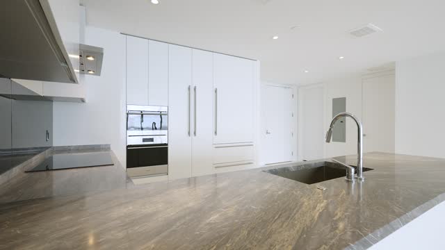 Modern design of white luxury kitchen with grey marble surface and contemporary technology. Glossy cabinet with built in household appliance, electric stove and oven