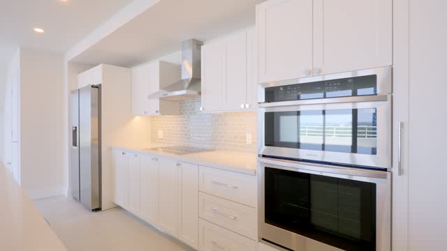Angle view on contemporary kitchen design in cozy penthouse with new built-in appliances from stainless steel. Bright dining room with marble island and halogen lights