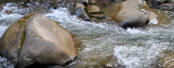 Photo of River flowing over rocks and boulders with white water and various shades of brown and gray rocks and boulders.