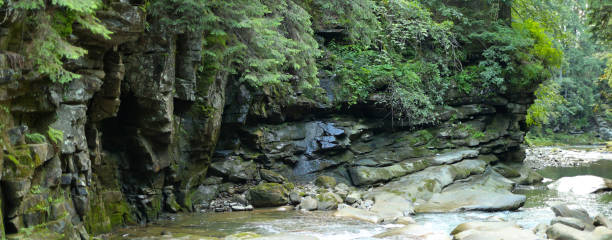 istock Rocky cliff face with a small waterfall and a stream at the bottom. The cliff face is made up of large, jagged rocks and is covered in moss and ferns 1583619649