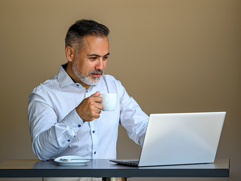 Portrait of a happy mature businessman standing at a table holding a cup of coffee