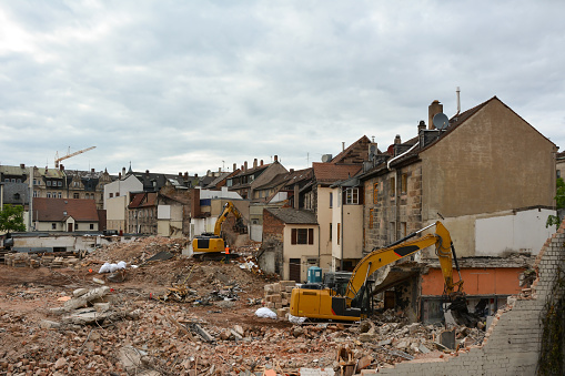 Several construction excavators are engaged in dismantling an old brick house. Dismantling the city's housing stock for renovation