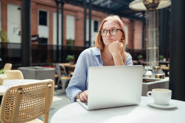 istock Stressed young blonde woman using laptop at cafe, sitting at table with notepad and cup of coffee alone 1583652305