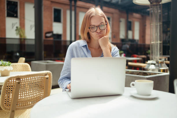 istock Stressed young blonde woman using laptop at cafe, sitting at table with notepad and cup of coffee alone 1583655931