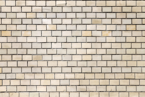 Close-up texture of an old, cracked and dirty wall made of beige rectangular tiles as a background