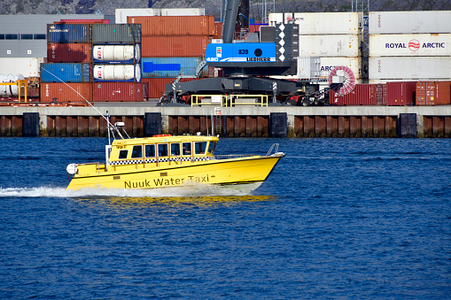 Nuuk / Godthåb, Greenland: Nuuk watertaxi speedboat Ice Force V, a Targa 37 vessel built in Finland, passing in front of Nuuk harbor container terminal (Fyrø island) - due to the absence of a road network, boats are crucial for passenger transportation along Greenland's fjord riddled coast - Nuuk bay.