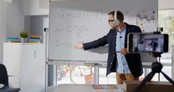 istock Senior positive online physics teacher writing on board with formulas having online class 1583691711