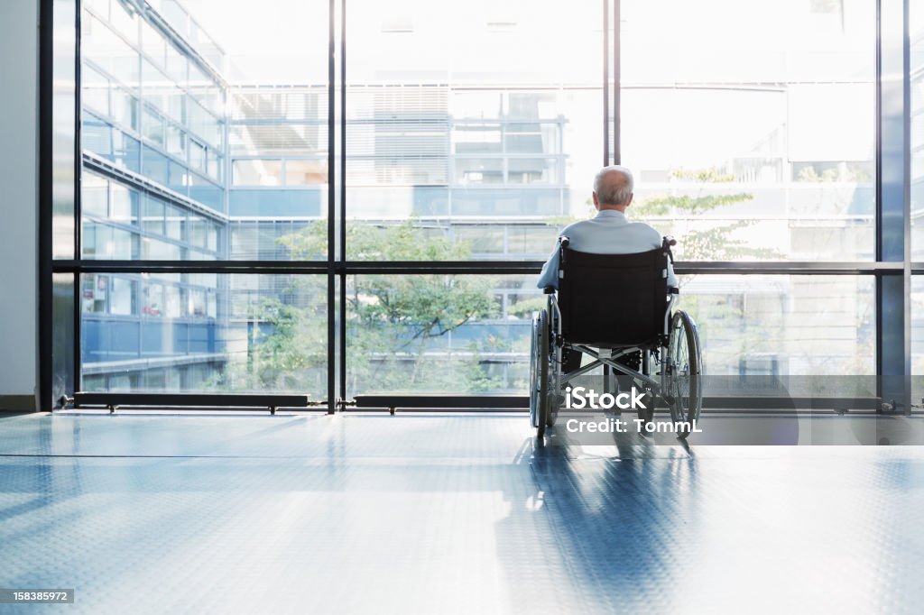 Senior Man in Wheelchair Senior Man in Wheelchair looking out of a window in a hospital corridor. Nursing Home Stock Photo