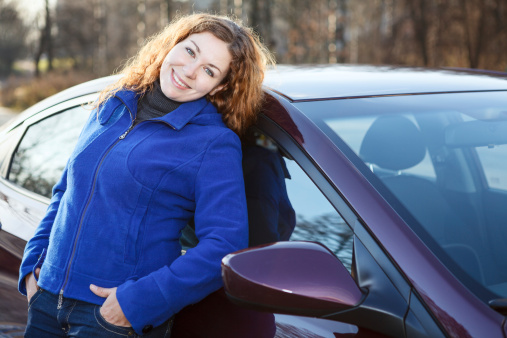 Beautiful woman leaned to car smiling and looking at camera