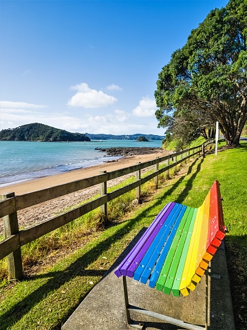 Paihia, New Zealand - July 1, 2023: A rainbow painted bench seat on the waterfront along Marsden Road on the Twin Coast Discovery Highway.