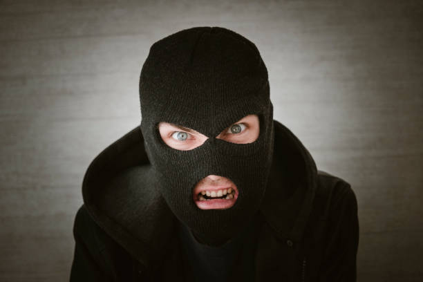 istock thief in a black jacket. A man in a black balaclava with an evil expression on his face. An aggressive bandit on a white background. The concept of crime or theft. 1583957083