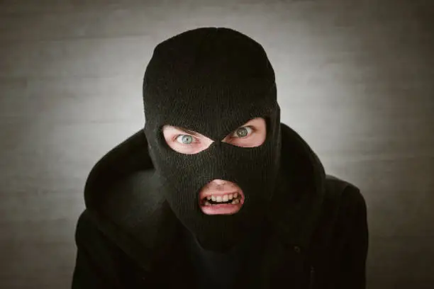 Photo of thief in a black jacket. A man in a black balaclava with an evil expression on his face. An aggressive bandit on a white background. The concept of crime or theft.