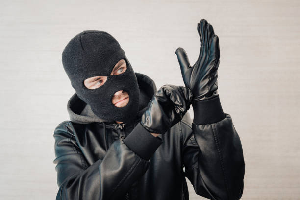istock thief in a black jacket. A man in a black balaclava with an evil expression on his face. An aggressive bandit on a white background. The concept of crime or theft. 1583957594