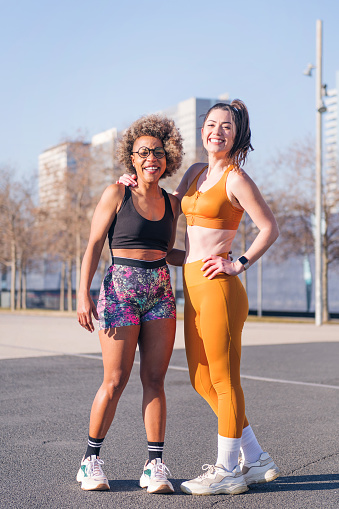 vertical portrait of two multiethnic sport friends smiling happy looking at camera standing on the city, concept of friendship and sportive lifestyle