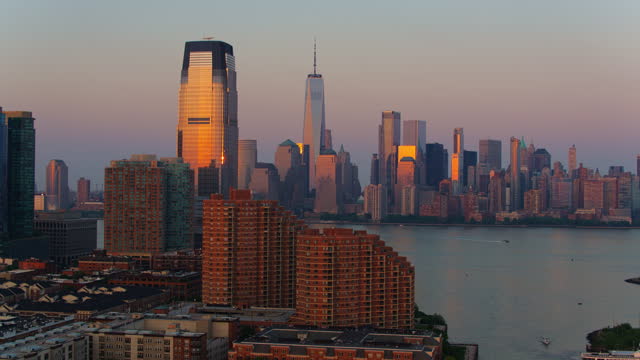 Boats are sailing on Hudson River between Paulus Hook, Jersey City and Lower Manhattan at sunset. Aerial video with the forward-descending camera motion.