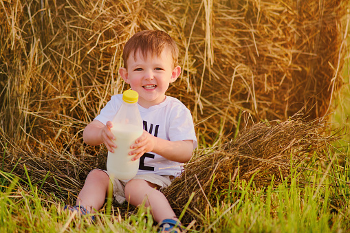 The child with bottle milk, a smiling boy , finds joy in the simple pleasures of childhood, surrounded by the beauty of nature and the farm's agriculture. Portrait of a happy kid aged two years