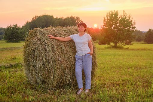 Nature of summer is captured in a portrait of a happy senior woman surrounded by hay bales. Portrait of a happy senior woman of sixty years