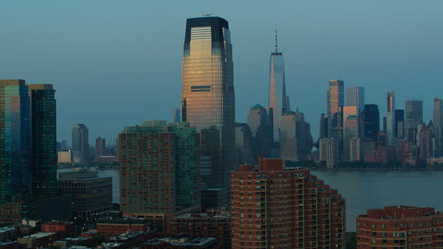 Downtown Manhattan with Freedom Tower distant view, over the Hudson River from Paulus Hook in Jersey City at sunset. Aerial video with the panning camera motion.