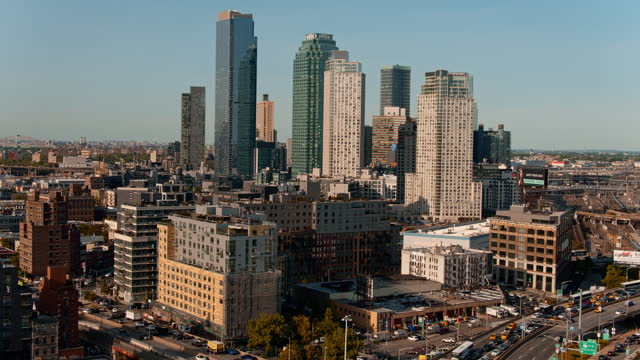 Modern office and residential buildings in Long Island City, Queens surrounded by older residential developments, on a sunny day in spring. Aerial video with the panning-wide-orbiting camera motion.