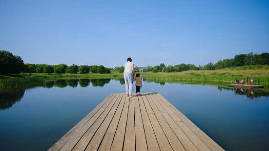 A child and his grandmother are having fun on the lake. On a wooden pier in the park, a child and a boy are happily playing. Kid aged two years