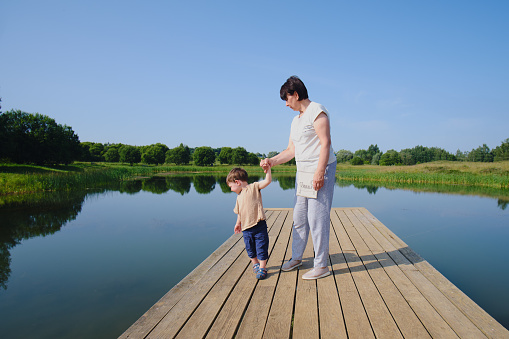 A real joy for a baby is a walk with his grandmother on the pier. The family is happily strolling along the wooden pier on the lake. Kid aged two years