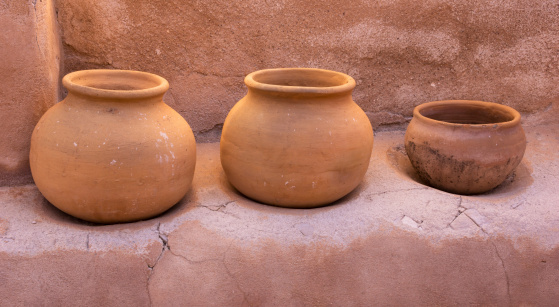 Three old terracotta clay pots sit side by side on an adobe ledge.