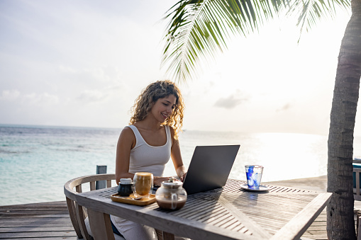 Happy woman working on her laptop while traveling and drinking a coffee - telecommuting concepts