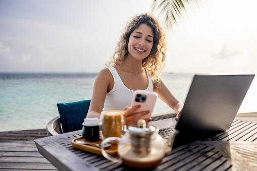 Happy nomadic woman using technology while working at a travel destination - telecommuting concepts