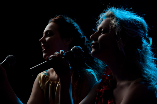 Two pretty women singing in microphone over the black background