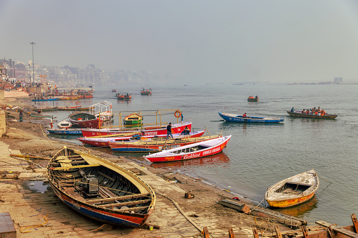 This is a photograph of numerous small boats, some with passengers, on the River Ganges in Varanasi, India, with the city itself in the background
