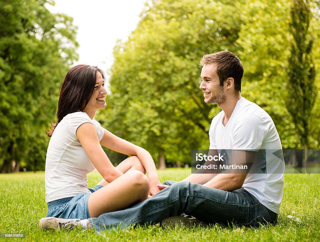 Young couple talking outdoor Young happy couple talking together outdoor - sitting on grass Adult Stock Photo