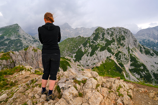 Back view of Senior woman on the top of Visevnik, the 2050 meter high peak, surrounded with mountains and cloudy sky. It is most visited 2000 and up mountain peak, starting from Plateau Pokljuka as it has good markings, easy path and it can be reached in two ours. The Karst Plateau is located in the Julian Alps at an elevation up to 1400 meters in northwestern Slovenia.