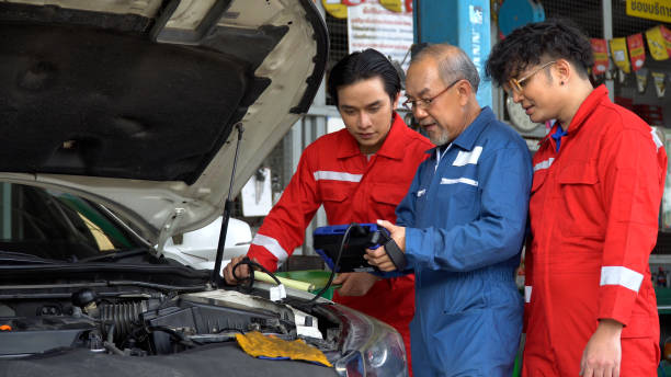 senior asian car mechanic manager training apprentice to checking car engine by Diagnostics Software repair in garage . old asia Auto mechanic teaching trainee or assistant on the repair shop . stock photo