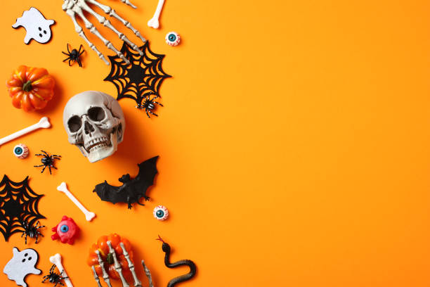 istock Halloween flat lay composition with skull, spiders, pumpkins, ghosts, skeleton hands on orange background. 1584425750