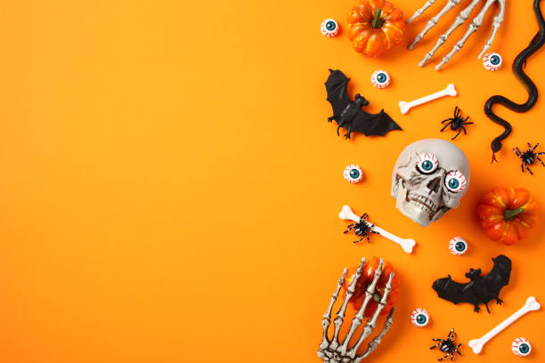 istock Happy Halloween flat lay composition. Pumpkins, bloody eyes, skeleton hands, bats, bones, skull on orange background. 1584427302